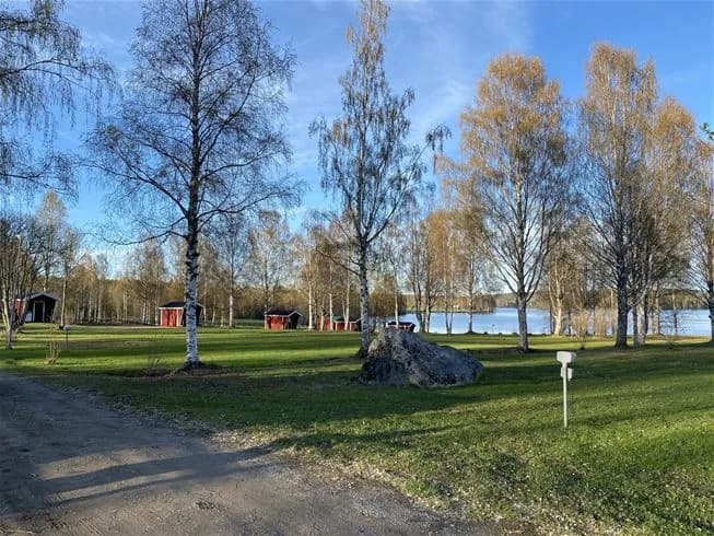 En öppen campingplats med gröna gräsmattor och glesa träd som ger skugga, omgiven av ett öppet landskap och en lugn atmosfär.