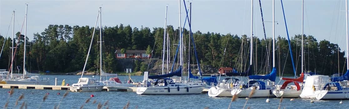 En grupp båtar förtöjda vid en marina med segelmaster synliga, omgivna av vatten i Arkösunds campingområde.