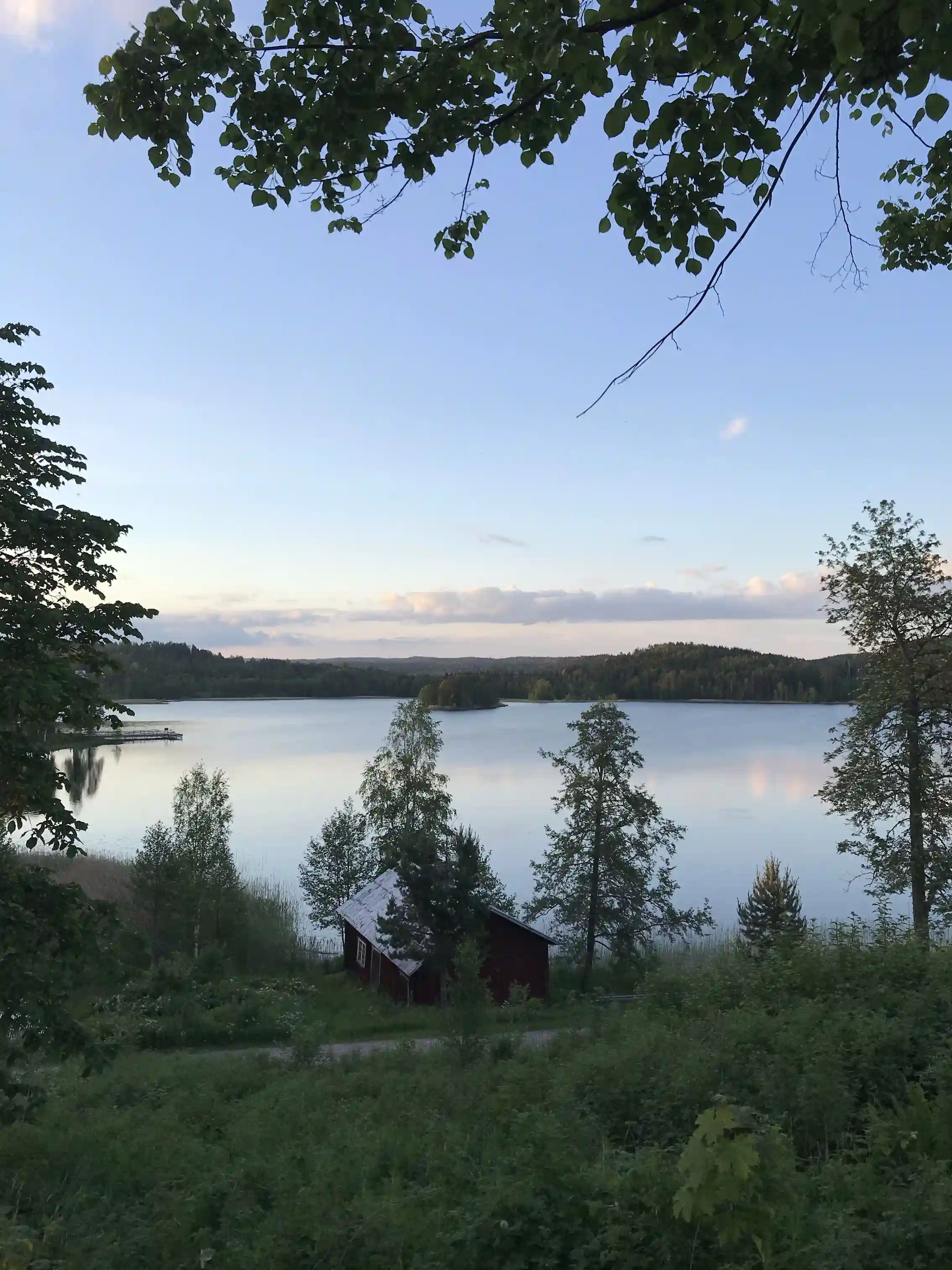 En lugn sjö vid Brunskog hembygdsgård omgiven av grönska och vildmark.