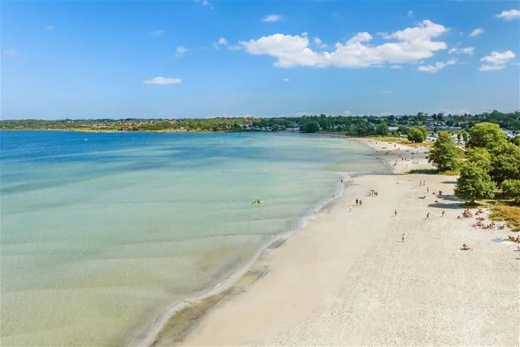 En strand med vidsträckt horisont, där sand möter havet under en molnig himmel.