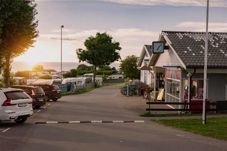 En campingplats med flera uppställda husbilar och bilar på en parkering. Molnig himmel ovanför.