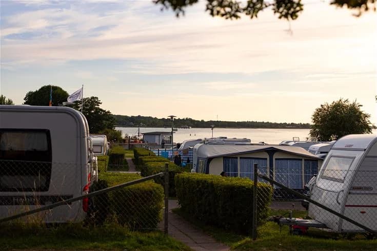 En husvagn står parkerad på Klinta Camping, omgiven av grönska och andra campingfordon.
