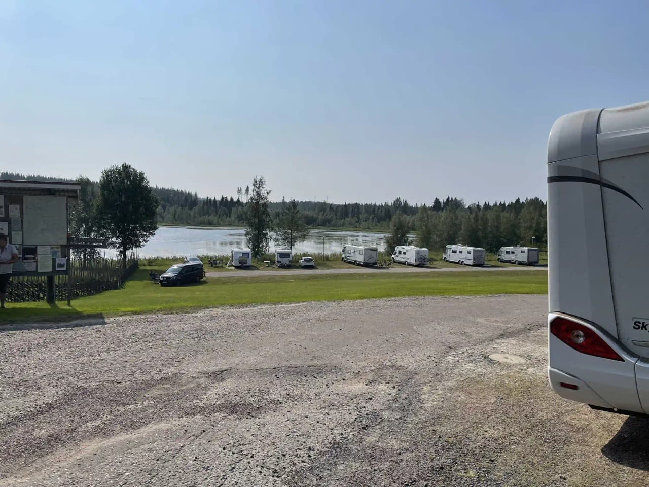 Bild av husbilar och husvagnar parkerade på en campingplats med molnig himmel i bakgrunden. Parkeringsområdet är öppet med flera mobila hem och fordon synliga.