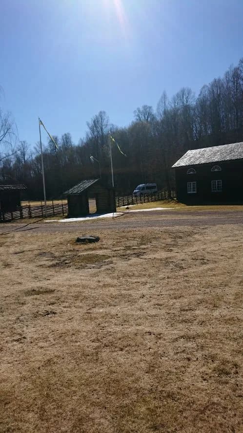 En lantlig vy av Gräsmarks hembygdsgård, med traditionella byggnader som lada och uthus omgivna av odlad mark och grönska.