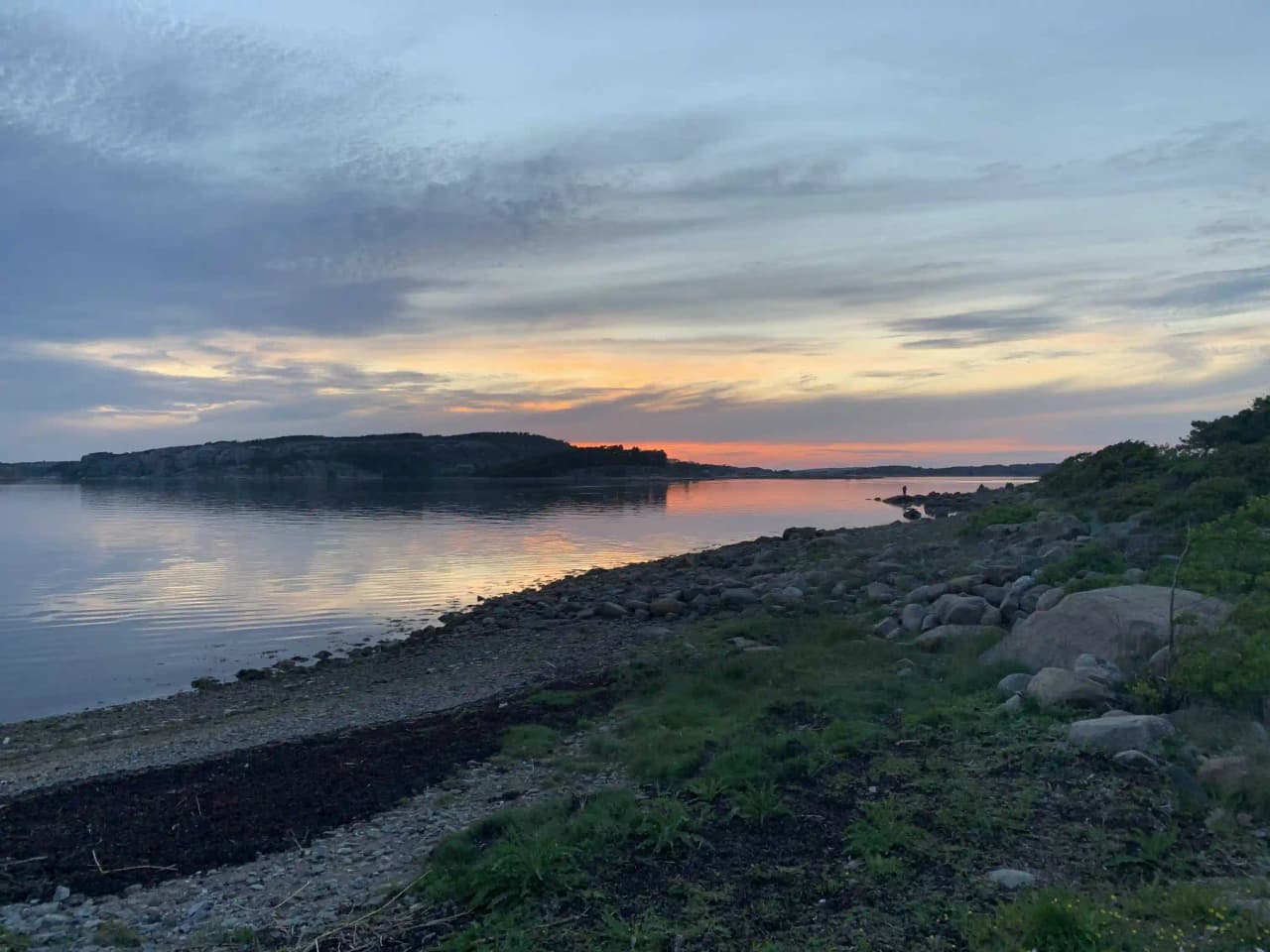 En vacker vy vid Fjällbacka camping med en glittrande vattenyta, omgiven av natursköna klippor under en skymningshimmel med lätta moln vid horisonten.