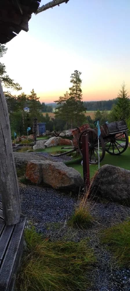 En grönskande trädgård på Lufta Camping & Restaurang med vackra landskapselement, höga barrträd och ett välskött grönområde under en klar himmel.