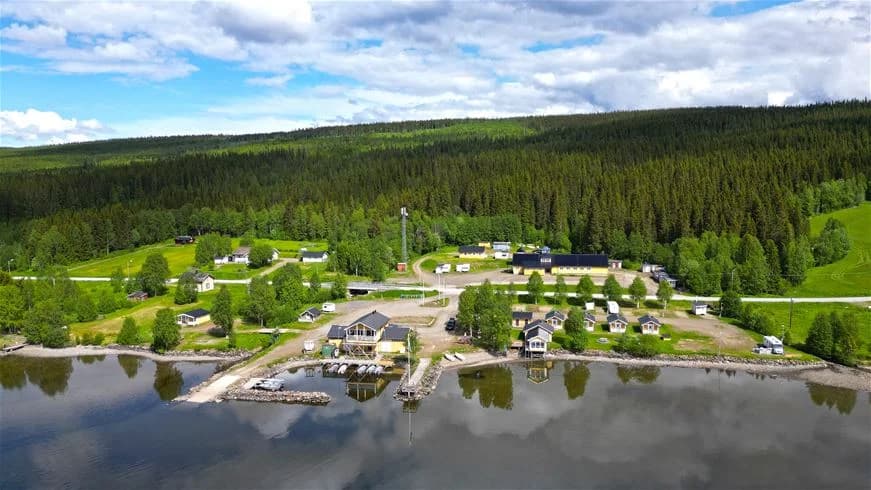 En mysig stuga vid stranden av ett glittrande vattendrag, omgiven av tät, vintergrön skog och omgivande floddalar, i ett naturskönt landskap som inbjuder till fiske och friluftsliv.