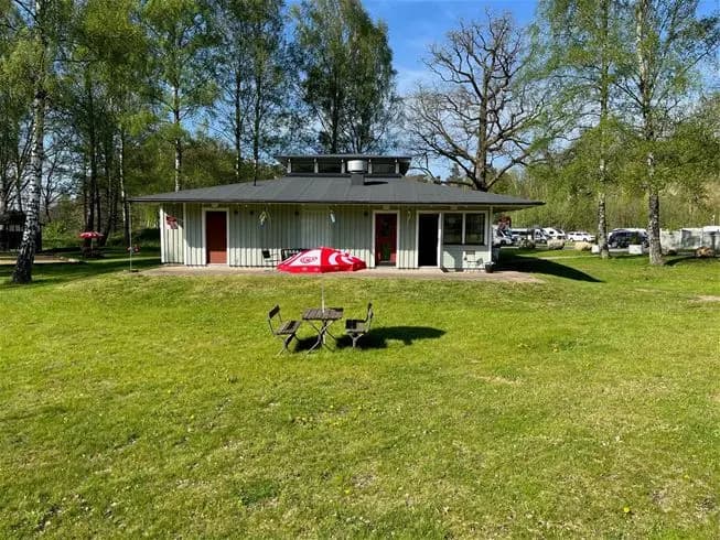 En mysig naturbild med en grön gräsmatta och lummiga träd som omger en röd stuga med vitt tak, belägen på Skäralids camping.