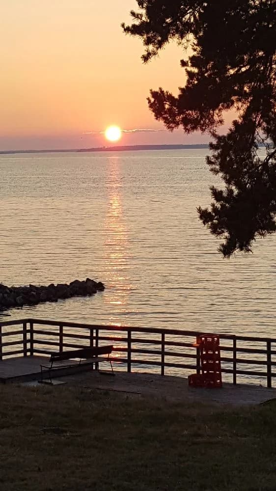 Ett vackert kvällslandskap vid Hjälmargården & Läppe Camping, där en solnedgång färgar horisonten i varma toner och speglas i det lugna vattnet.