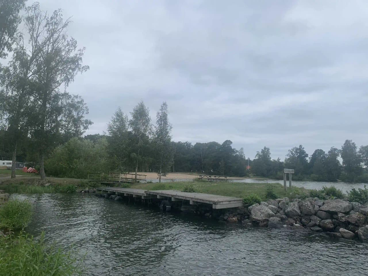 En naturskön vy över Hjälmargården & Läppe Camping, med en sjö omgiven av frodig grönska och träd.