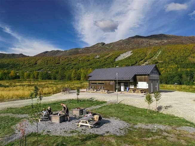 En pittoresk hydda omgiven av ett bergigt landskap i Kittelfjäll, Sverige, där vidsträckta gräsmarker och kuperade höjder dominerar vyn, vilket erbjuder en lugn och naturskön miljö.