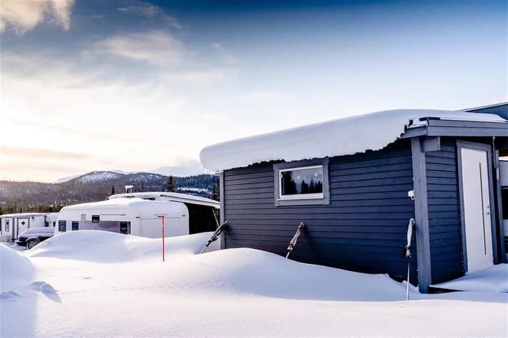 En vintrig landskapsbild av Camp Kittelfjäll med en stuga omgivet av snötäckta sluttningar och frusna isbildningar, fångar den arktiska stämningen.