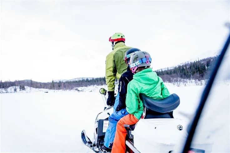 En snöskoterförare iklädd vinterkläder, hjälm och skidglasögon kör på ett snöklätt landskap i Kittelfjäll, perfekt för vinteraktiviteter och rekreation.