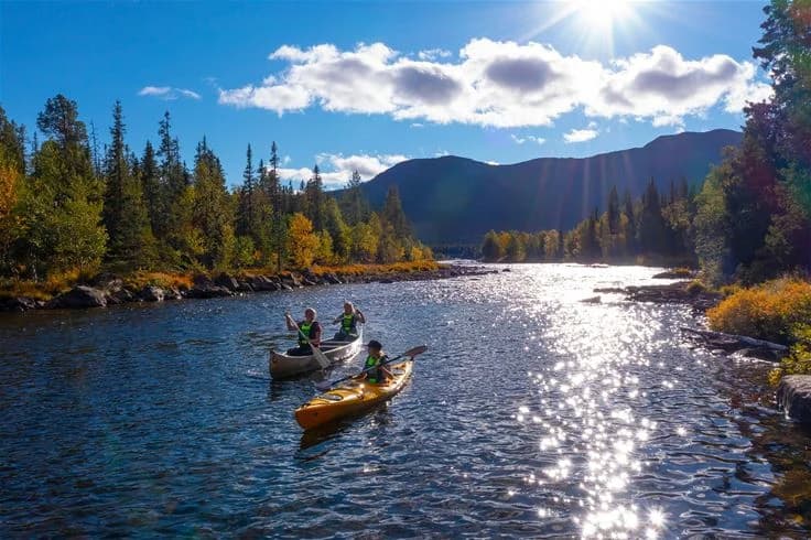 En paddlare i kajak på en stilla sjö omgiven av vild, orörd natur vid Camp Kittelfjäll.