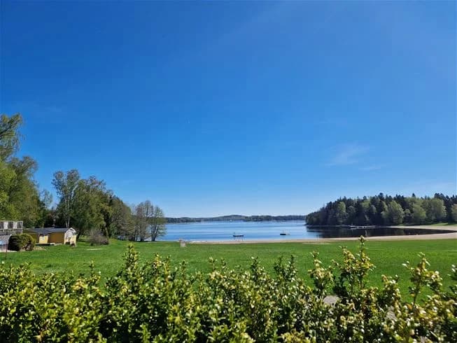Vy över det vackra landskapet vid Farstanäs camping & havsbad, med en klar blå himmel ovanför gröna ängar som sträcker sig mot horisonten.