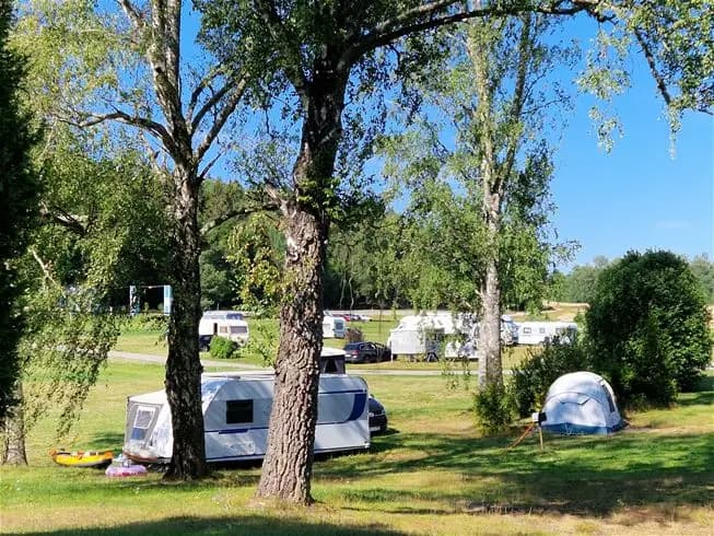 En campingplats vid Farstanäs Camping & Havsbad med husbilar och tält uppställda på grön gräsmatta. Träd omger området och skapar en lugn, naturnära miljö.