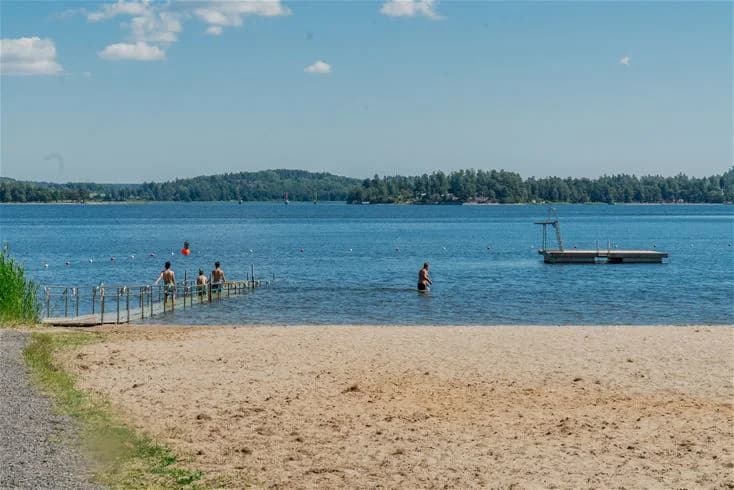 Vy över Farstanäs camping & havsbad med solig strand och glittrande hav. Perfekt plats för sommarrekreation.