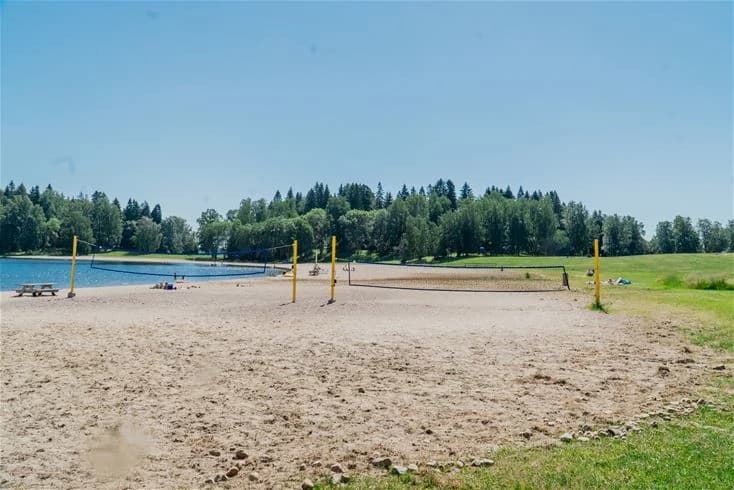 En sandstrand vid Farstanäs Camping & Havsbad med utsikt över en lugn sjö och omgivande grönområden.