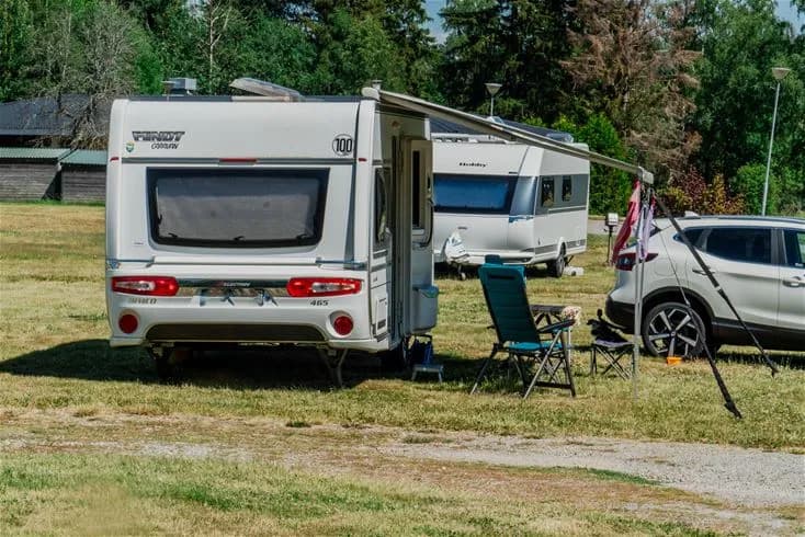 Bild av en husvagn och en husbil parkerade på Farstanäs camping & havsbad, omgivna av grönska i en avkopplande campingmiljö.