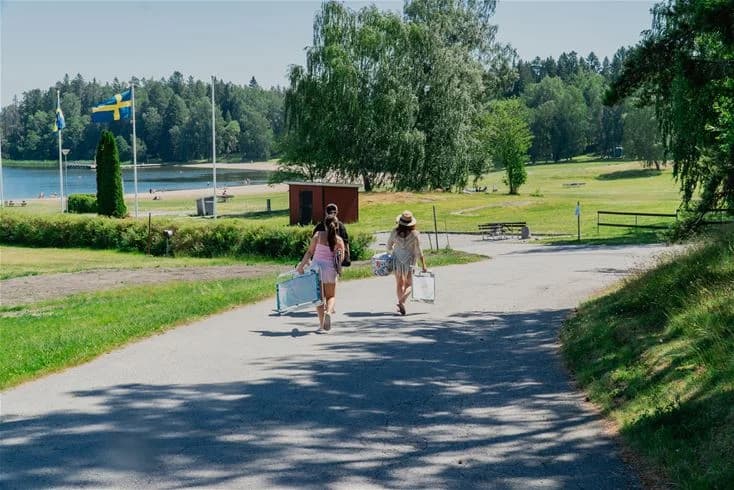 En grönskande campingplats med gräsbevuxna ytor och träd i bakgrunden, idealisk för rekreation och friluftsliv, med känsla av vårens spirande miljö.