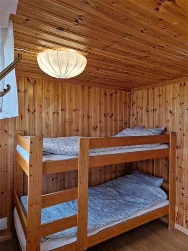 En rustik och hemtrevlig campingstuga med trägolv och träinredning. Stugan är möblerad med en enkel säng klädd i vita lakan, och har en varm atmosfär av träpaneler på väggar och tak.