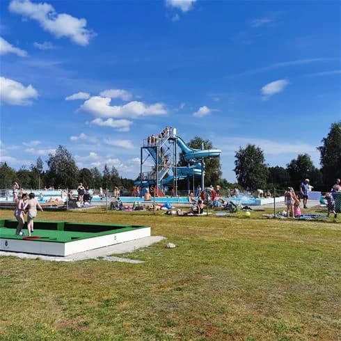 En klarblå himmel med några vita moln över en grönskande park vid Hede Camping, där personer njuter av fritid och rekreation i en naturskön miljö.