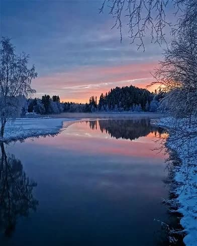 En stilla sjö vid Hede camping i skymningen, med blått vatten och omgivande natur. Solnedgångens glöd reflekteras på ytan, vilket ger en fridfull och naturskön atmosfär.
