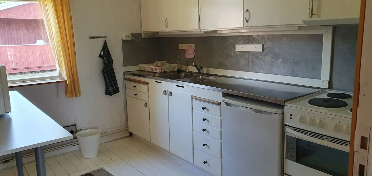 Bild på köket i Stigmansgården, Tiveden. Köket har trägolv, träbänkskivor och träskåp. Det finns även stora köksapparater inklusive diskbänk och kylskåp, vilket bidrar till en hemtrevlig och rustik inredning.