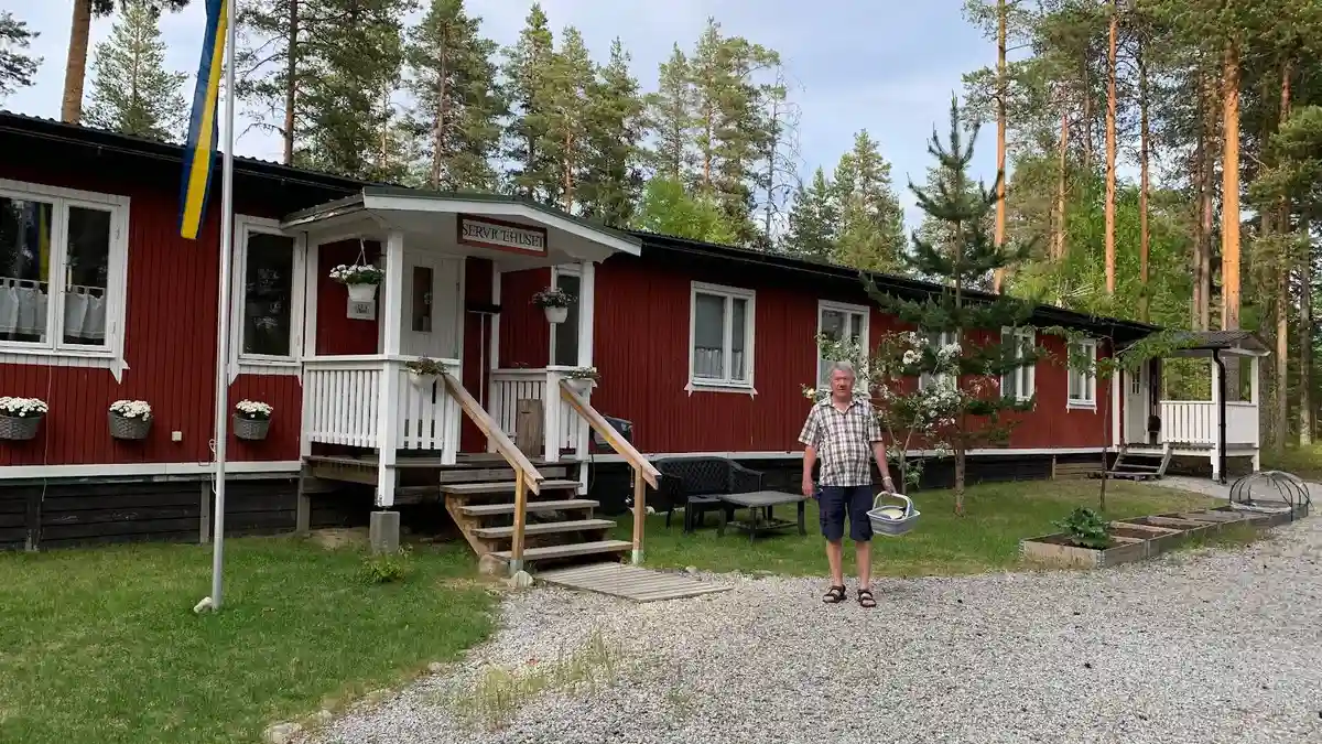 En mysig stuga utanför Lapplandsportens camping, med en veranda möblerad med utemöbler och omgiven av en grönskande gårdsplan.