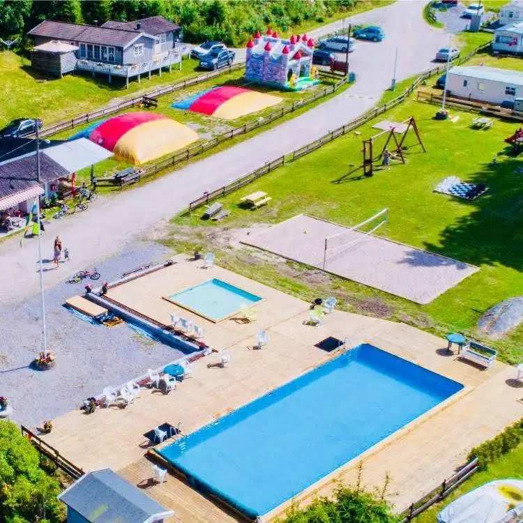 Flygbild över Ylserød camping, med en stor pool, omgiven av gröna områden, husvagnar och semesterfaciliteter i en semesterortsatmosfär.