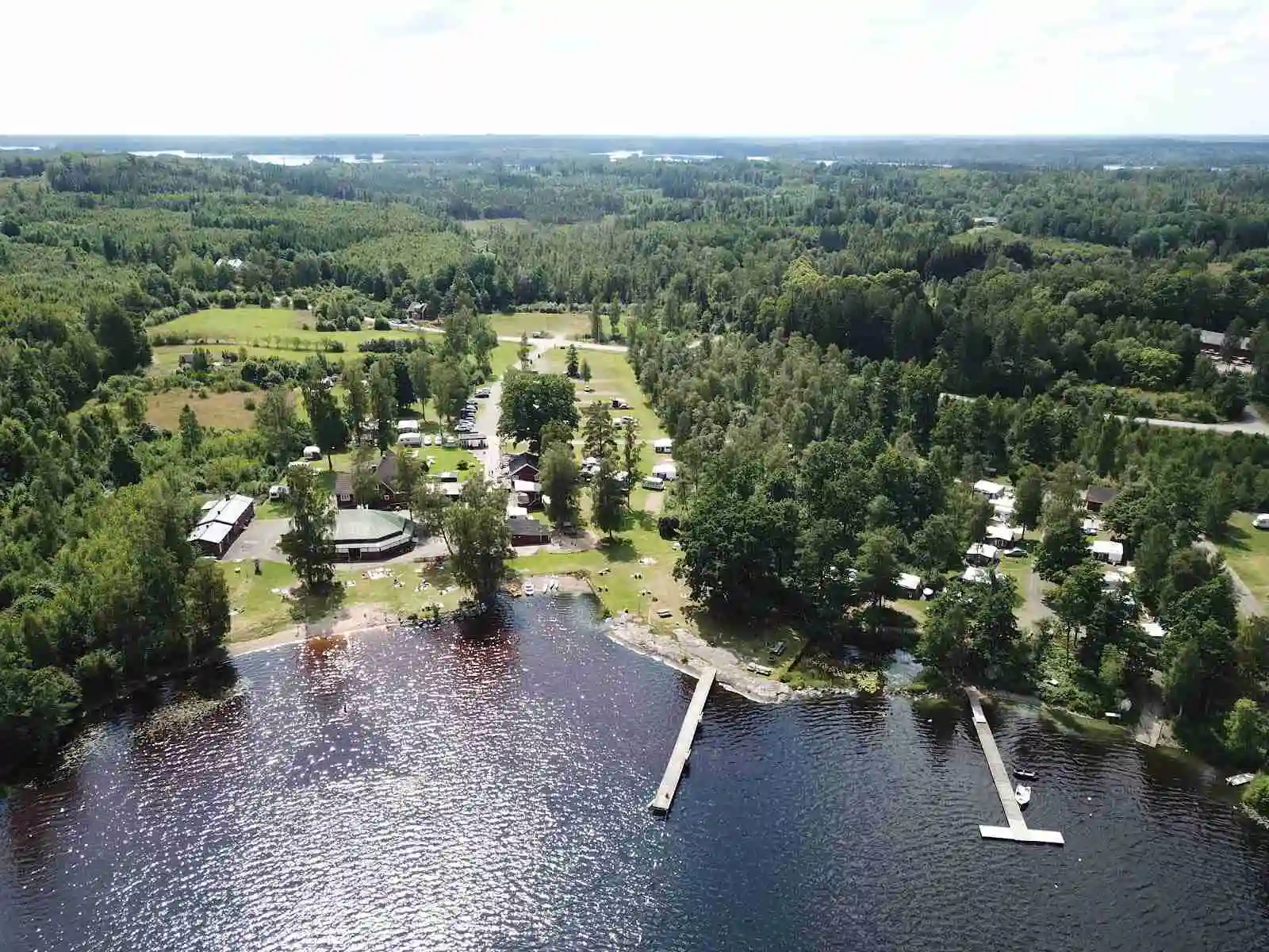 Flygfoto över Hätteboda vildmarkscamping visar ett naturskönt landskap med frodiga träd som omger en stilla sjö. En kanal sträcker sig genom området, vilket skapar en fridfull miljö för naturälskare.