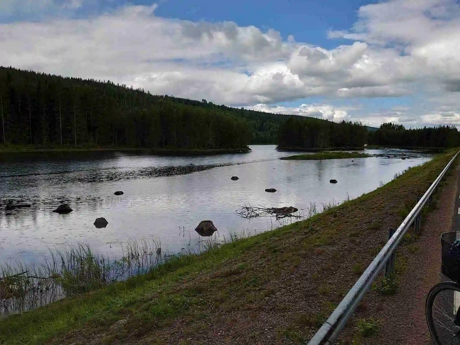 Vy över en naturskön sjö med omgivande landskap vid Nya Skogsgården, under en molnig himmel.