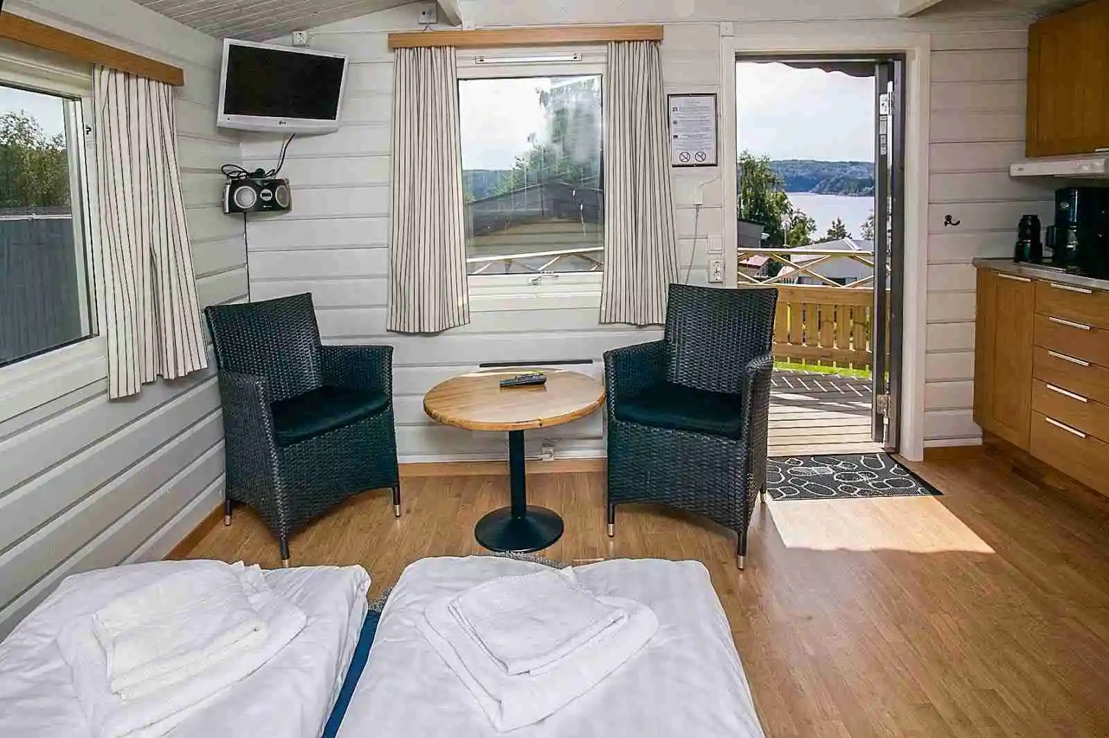 Bilden visar en mysig stuga vid Hafsten Resort & Camping, omgiven av lummig natur och byggd med träpaneler. Stugan ser inbjudande ut, idealisk för en avkopplande semester mitt i naturen.