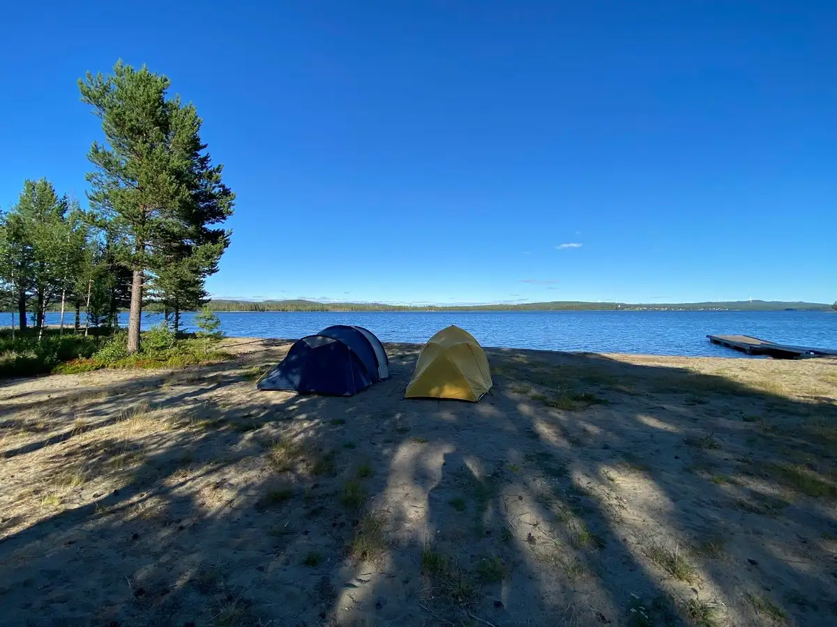 En kustnära campingplats vid en sjö med ett blått vatten och vidsträckt kustlinje, omgiven av naturskön landskap för rekreation och utomhusaktiviteter.