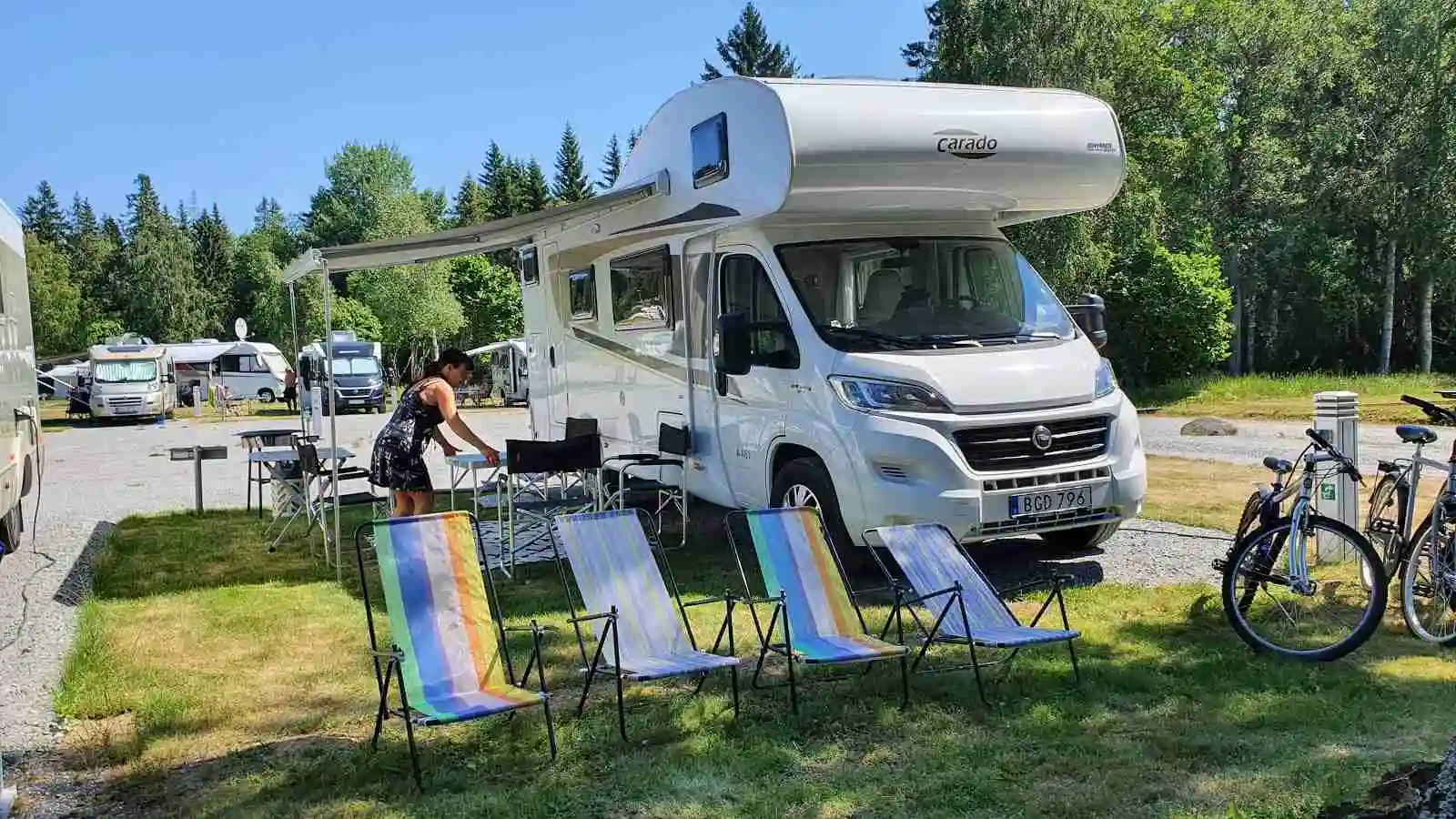 En husbil och en husvagn står parkerade på Kapellskärs camping, omgivna av grönska och träd.