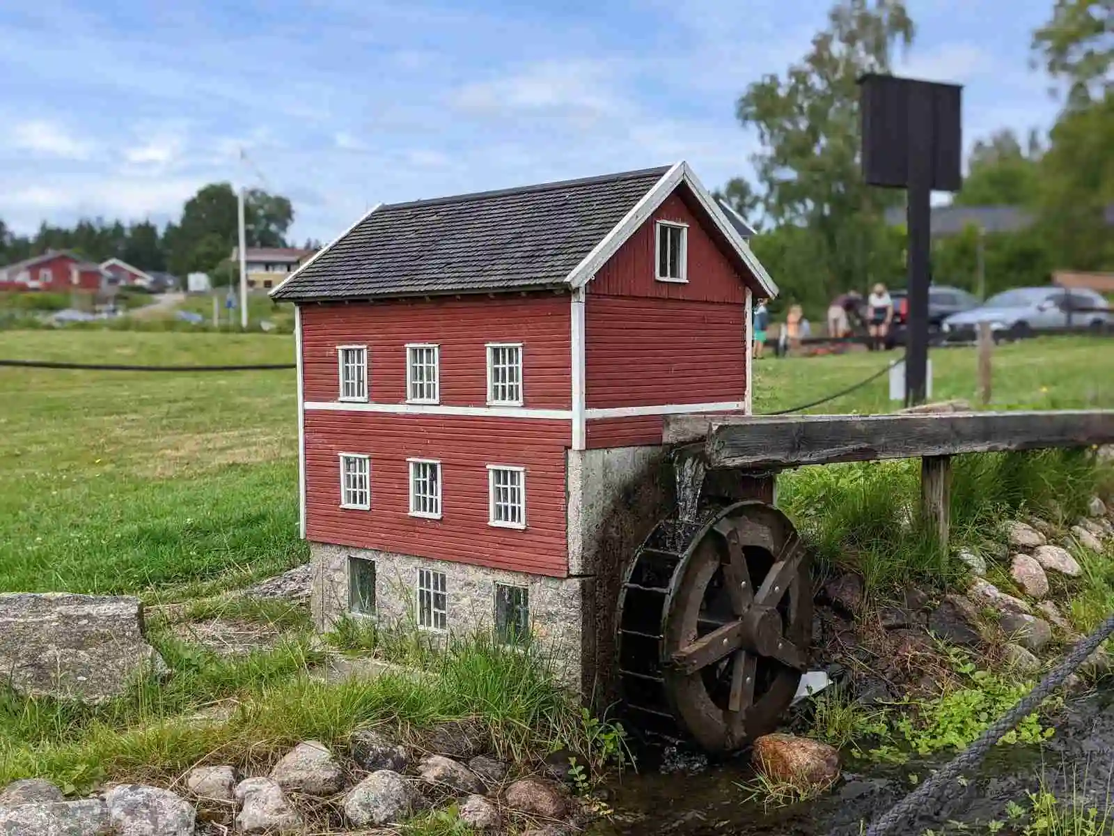 En mysig stuga vid en grönskande trädgård nära en kanal och våtmark, med en damm och ett förråd i bakgrunden, på Vegby Camping.