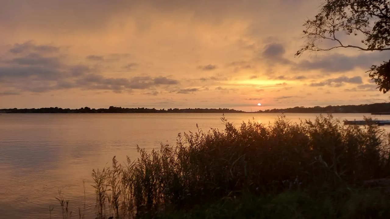 En vacker solnedgång över ett stilla hav vid Kustgården Senoren, med horisonten i fjärran och en färgglad himmel som speglas i vattnet.