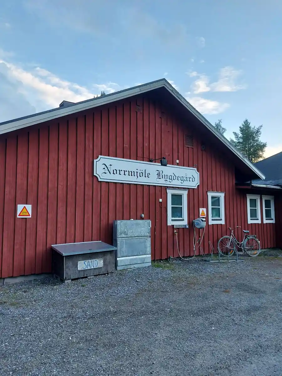 En välskött campingplats med grönskande gräsmatta och byggnader med ljusa fasader i trä.