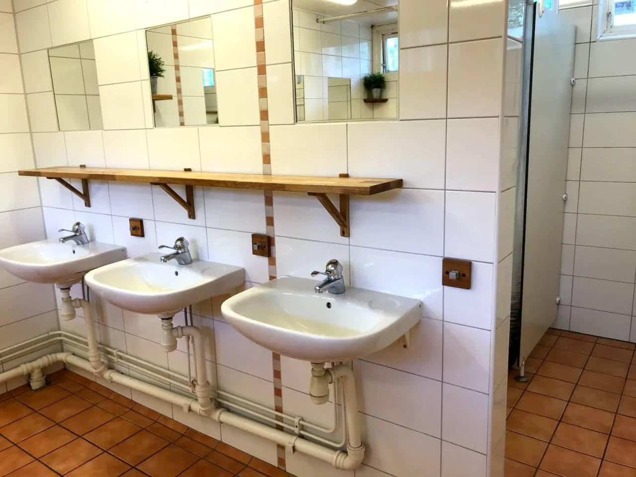 Bild av ett badrum på Lomma Camping med ett handfat och blandare. Rummet har ljusa kakelplattor på golvet och väggarna, skapar en ren och enkel design.