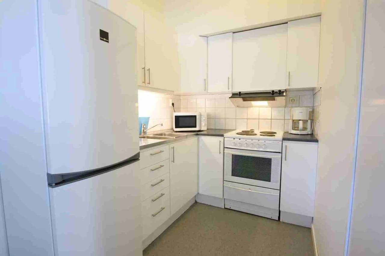 Ett modernt kök i en campingstuga på Östersunds camping med utrustning som vitvaror, diskbänk, bänkskivor och skåp. Ljust golv och tak skapar en inbjudande atmosfär.