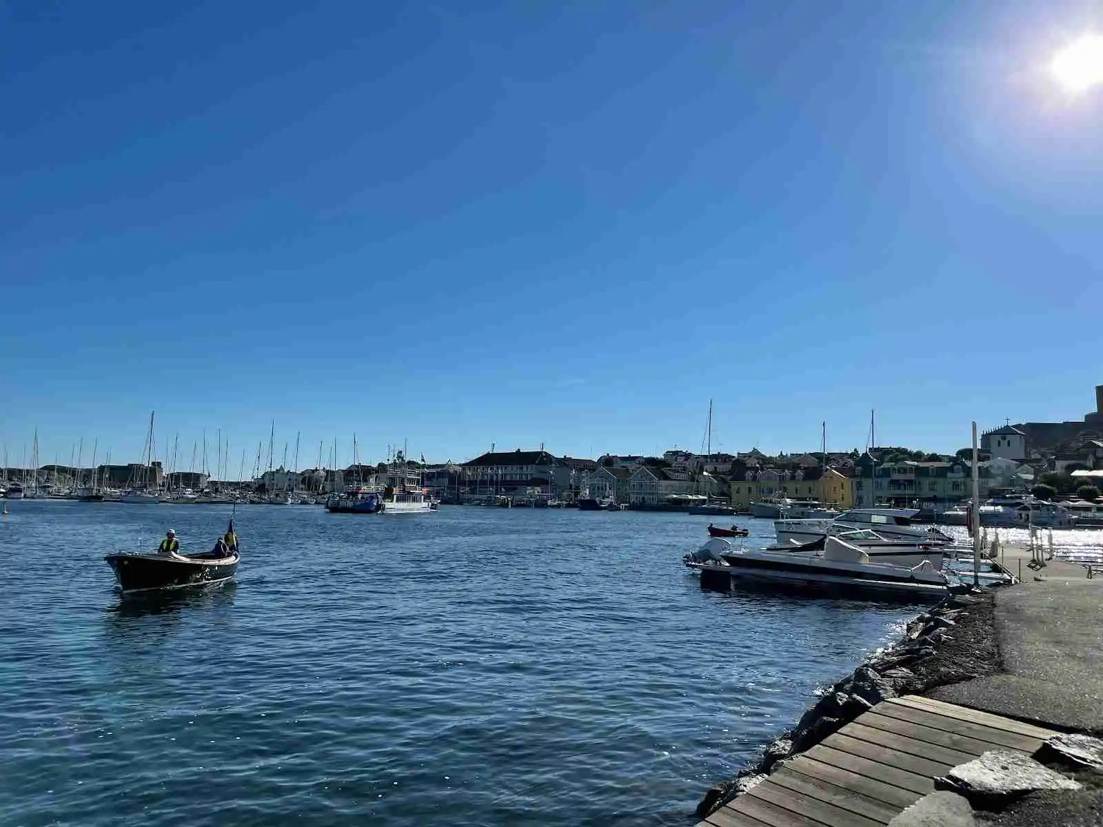 En marina vid Marstrands familjecamping med flera båtar förtöjda vid bryggorna. Vattnet i kanalen är lugnt, och havet syns i bakgrunden.