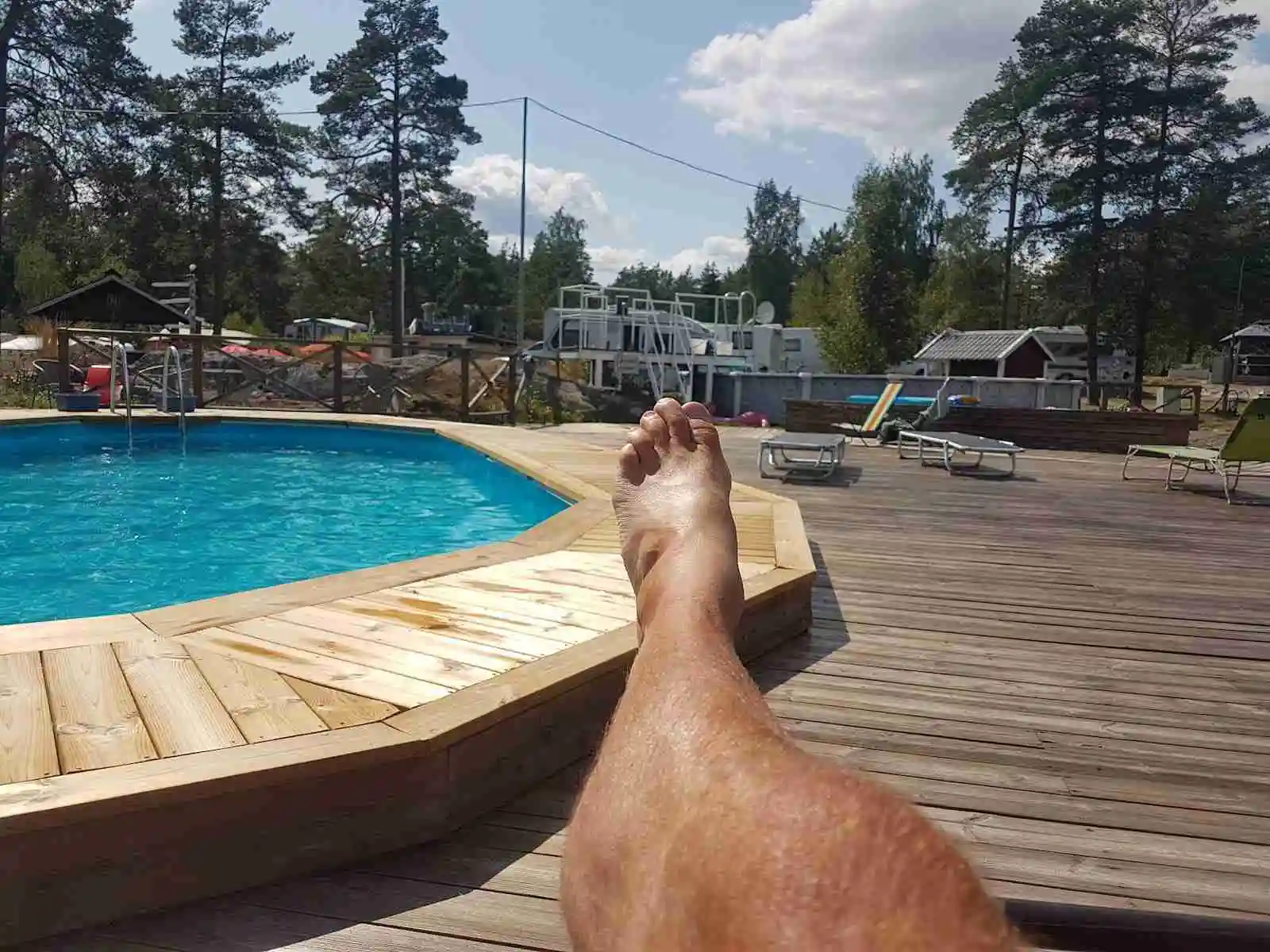En soldränkt campingplats vid Arkösunds camping med pool, solstolar och parasoller, omgiven av grönska och fritidsaktiviteter.