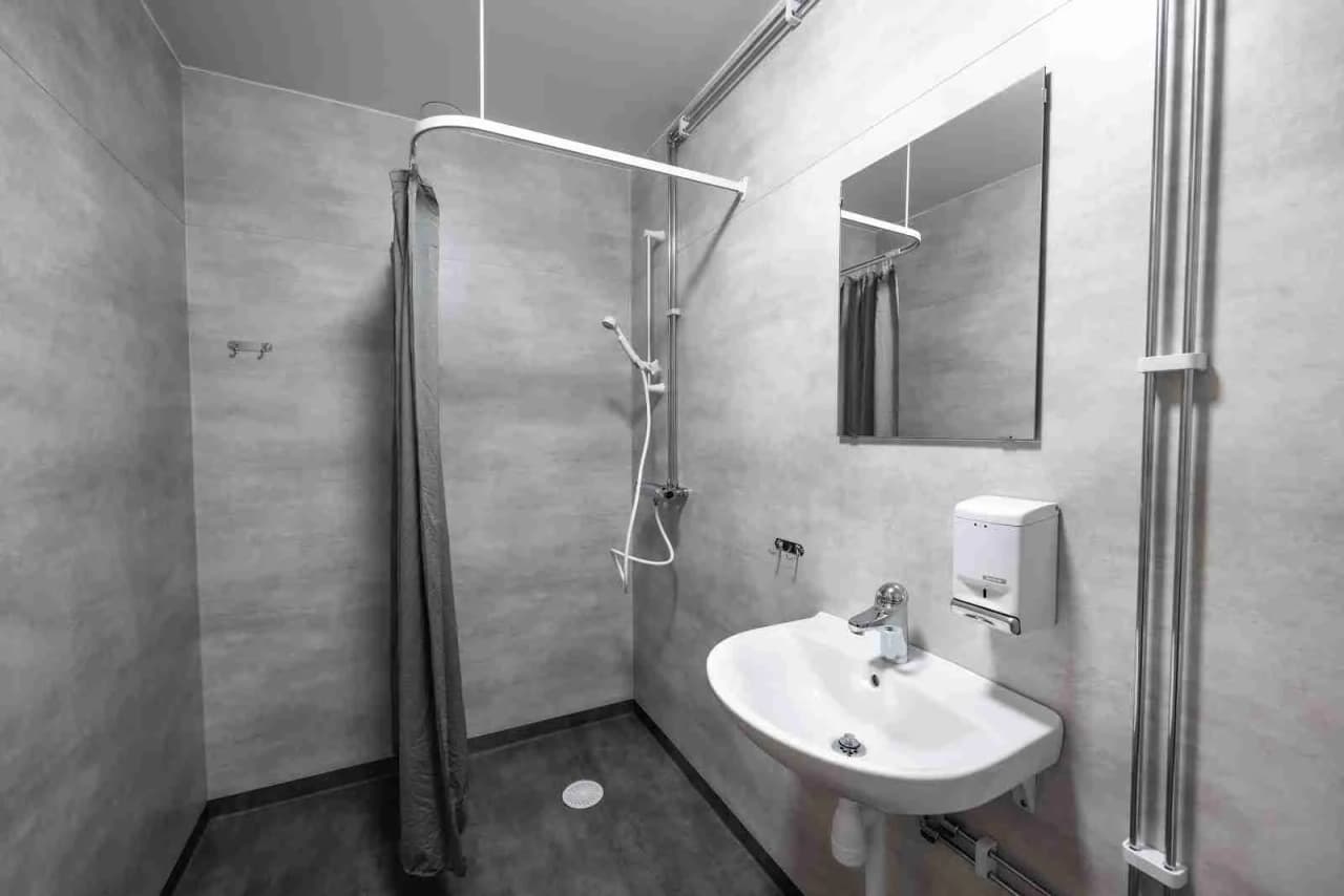 Interiör av ett modernt badrum på Östersunds camping med klinkergolv, en dusch och ett handfat med kranar.