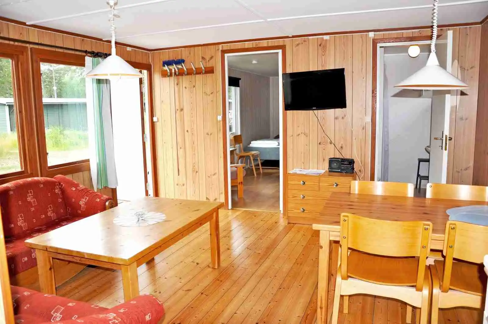 En varm och inbjudande interiör med träpaneler, trämöbler och träbord som ger en rustik känsla. Trägolvet och det vita taket kompletterar det naturliga temat, vilket skapar en mysig atmosfär idealisk för avkoppling och umgänge.