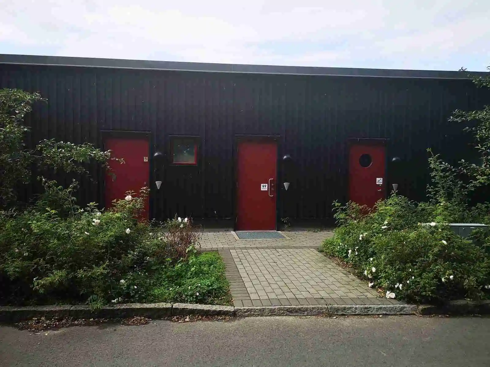 En solig trädgård vid mötesplats Borstahusen med en välskött uppfart av betong och frodig grönska samt en gångväg som löper genom landskapet.