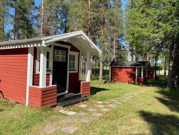 Bild av Vuollerim Camping med trästugor omgivna av grönska. Stugorna står intill en välskött trädgård, vilket ger en inbjudande och hemtrevlig atmosfär i naturskön omgivning.