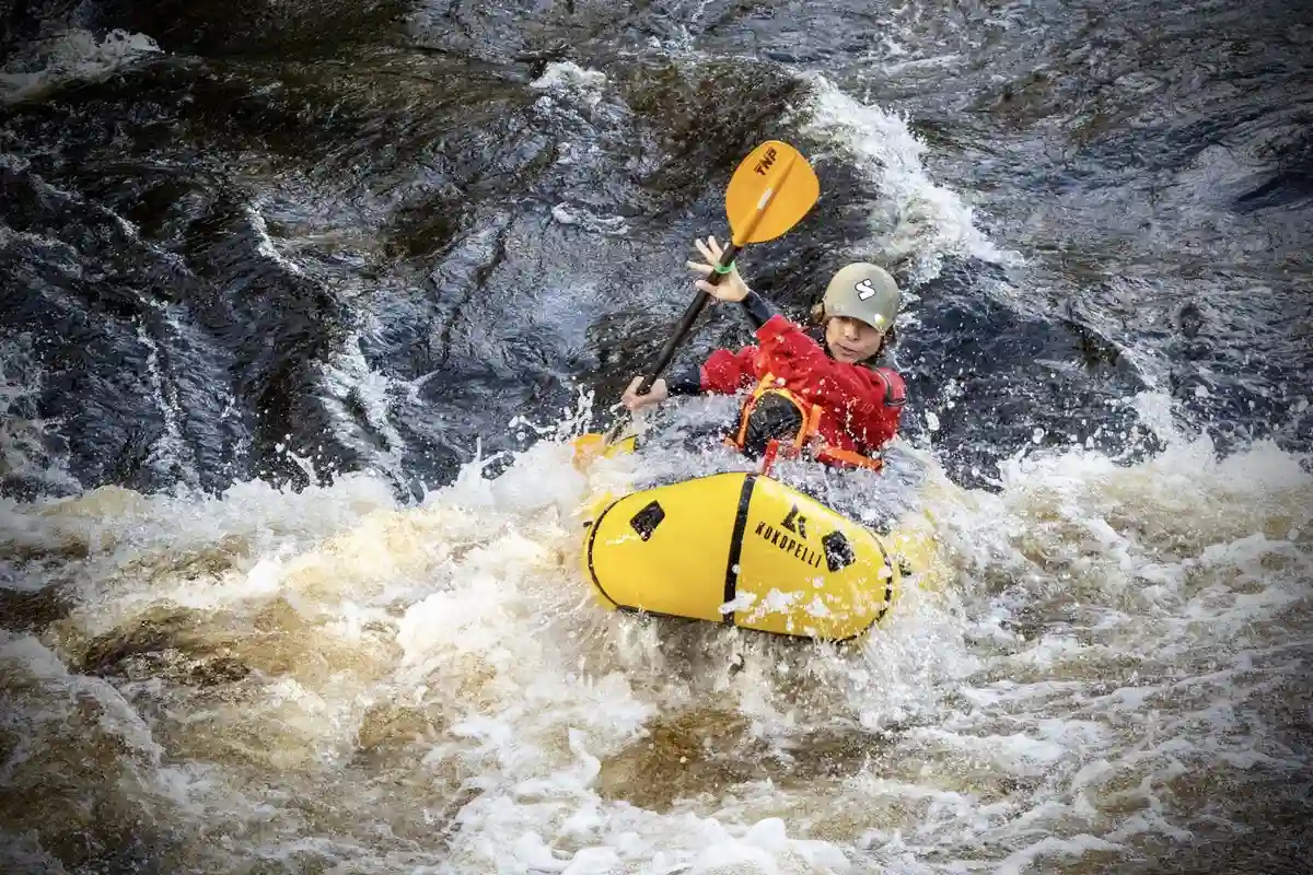 Alt-text: Person paddlar en kajak på en lugn vattenström, omgiven av grönska, med personlig skyddsutrustning avsedd för paddling.