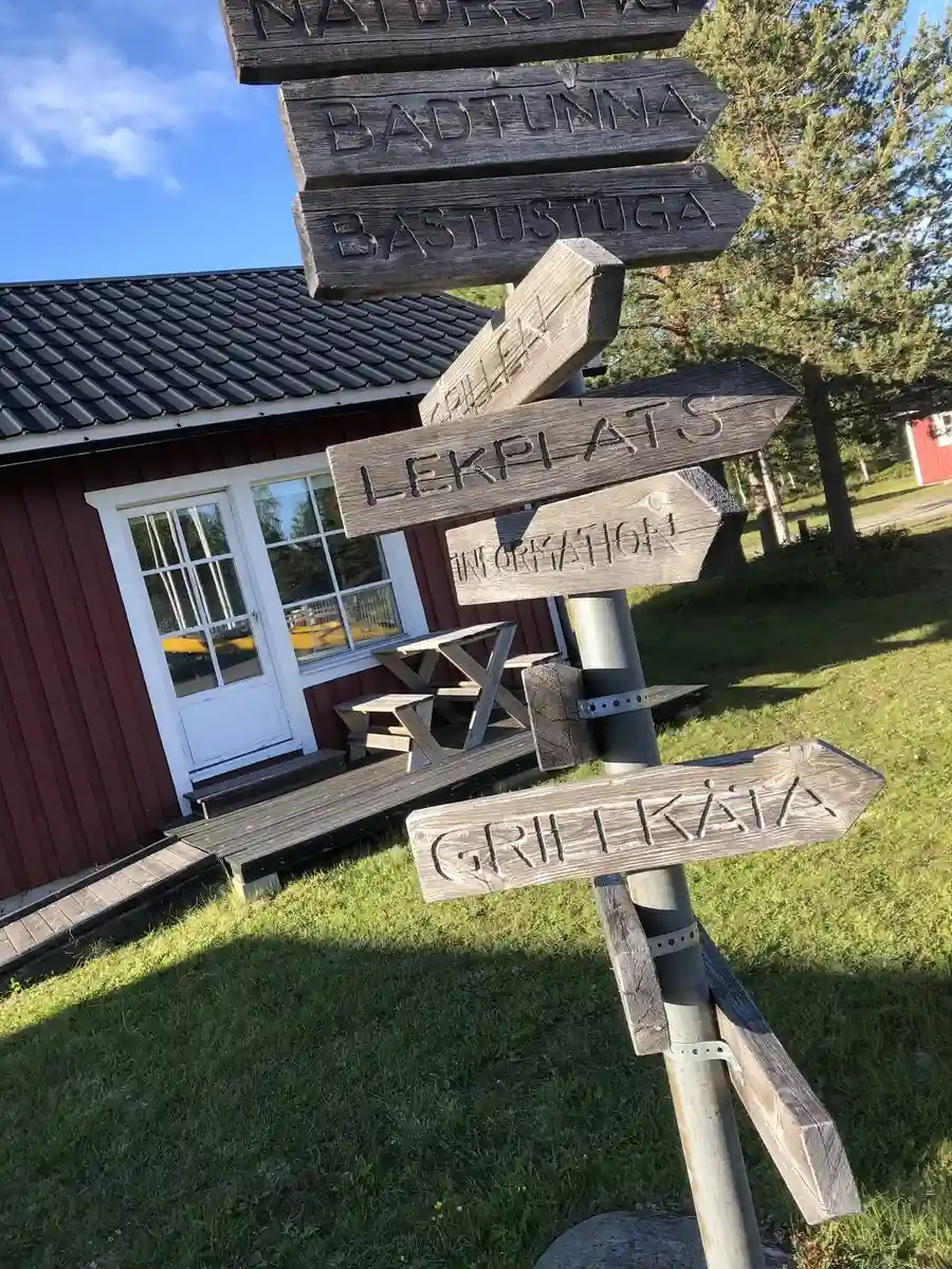 En blå gatuskylt med texten "Seskärö Havsbad & Camping". Omgiven av lummig grönska under en klar himmel.
