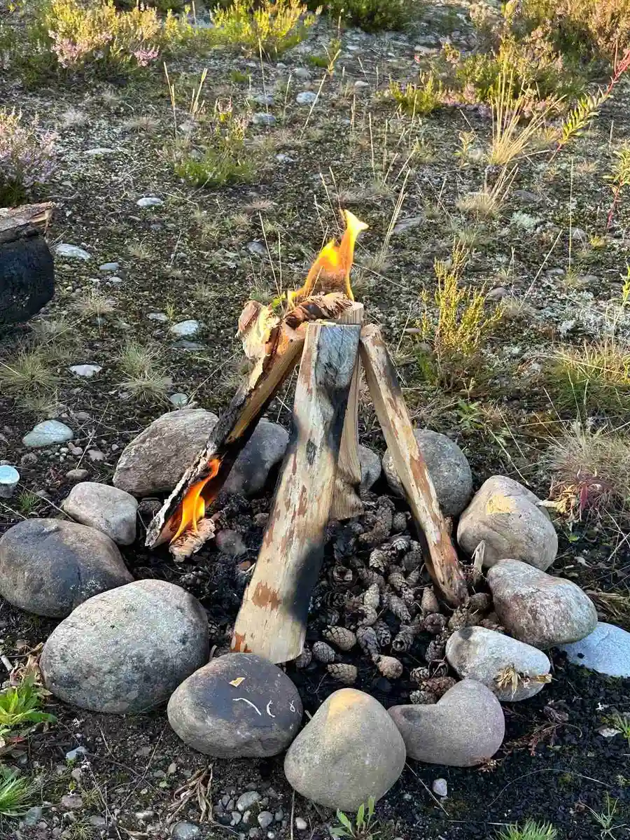 En närbild av en lägereld på Bråtens Camping, där eldslågor dansar över glödande kol och stenar i bakgrunden.