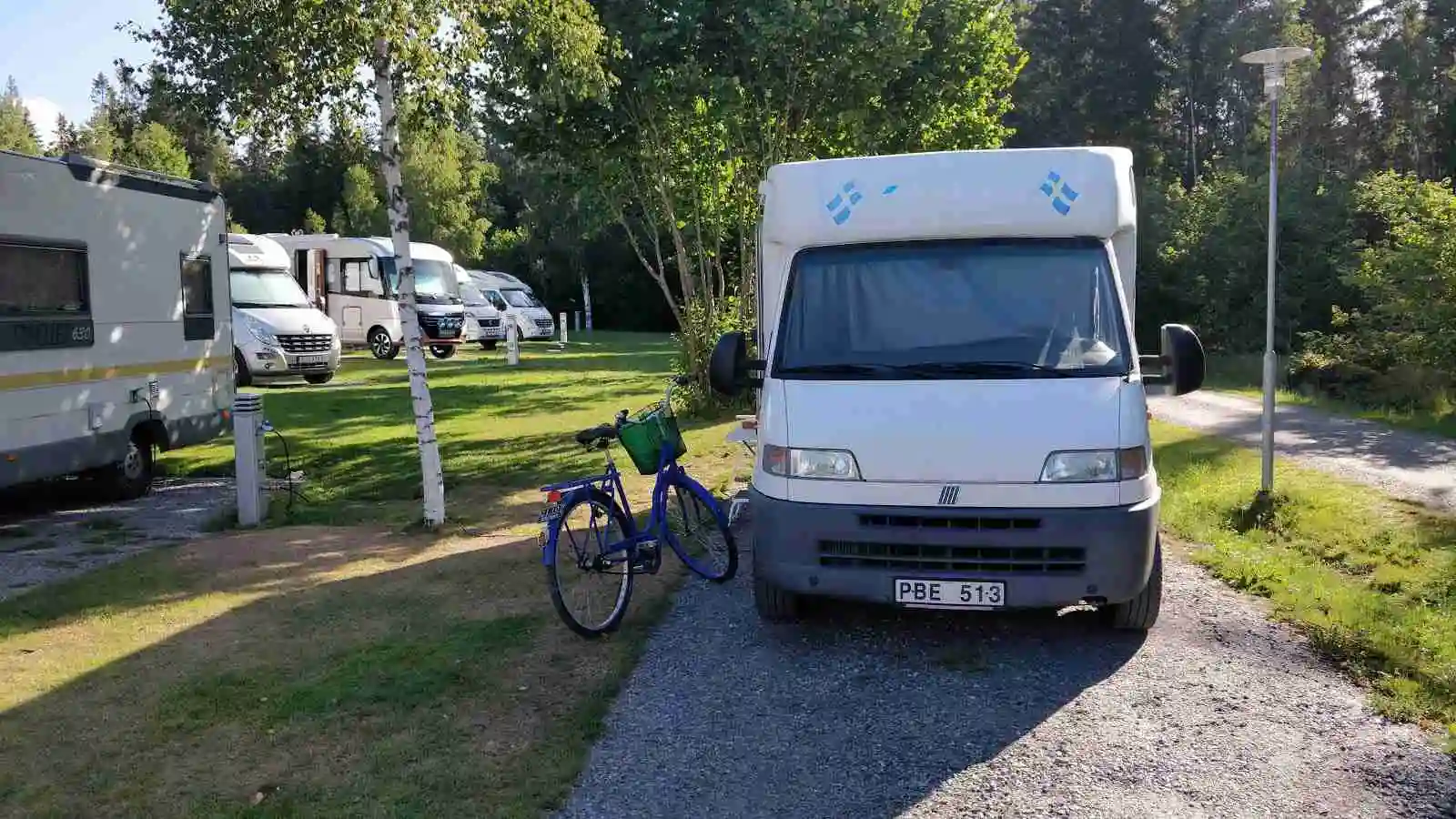 En husbil parkerad på en campingplats vid Kapellskärs Camping, omgiven av grönska och campingutrustning.